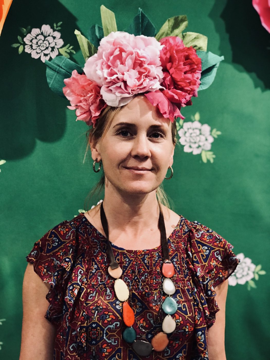 Amy wearing a crown of pink flowers and a beaded necklace against a green wall.