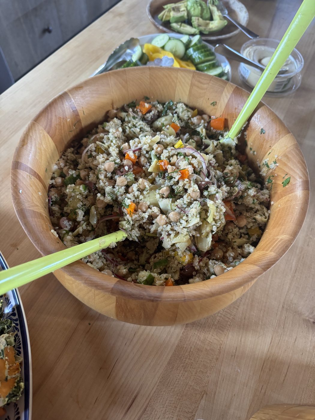 A wooden bowl of quinoa salad with roasted vegetables and herbs.