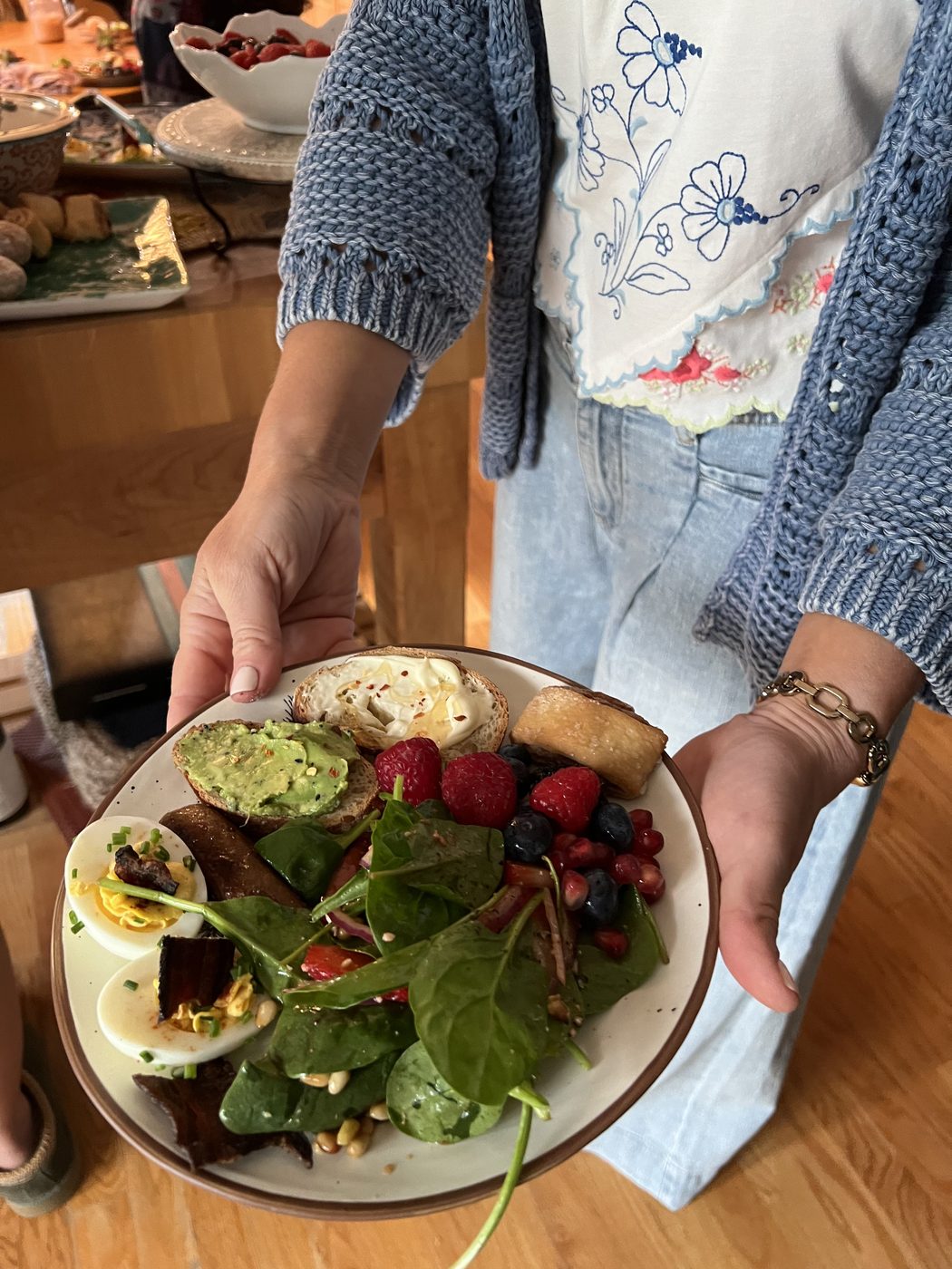 A guest holding a plate of greens, berries, avocado and deviled eggs.