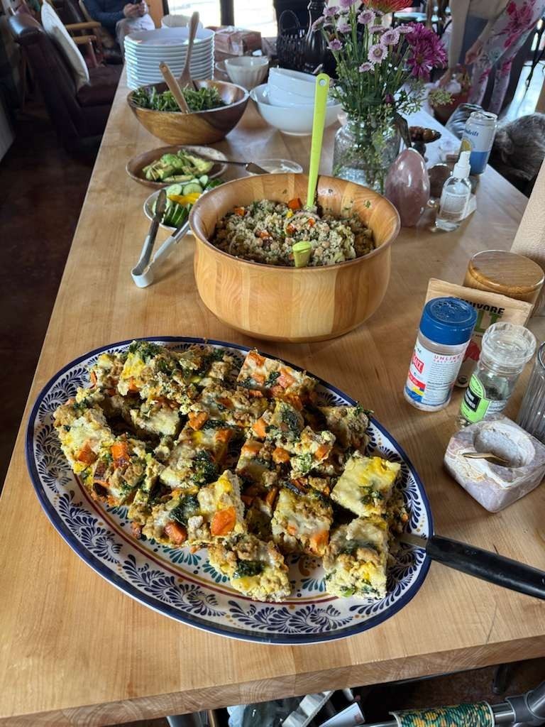 A buffet table with a vegetable frittata, quinoa salad and fresh flowers.