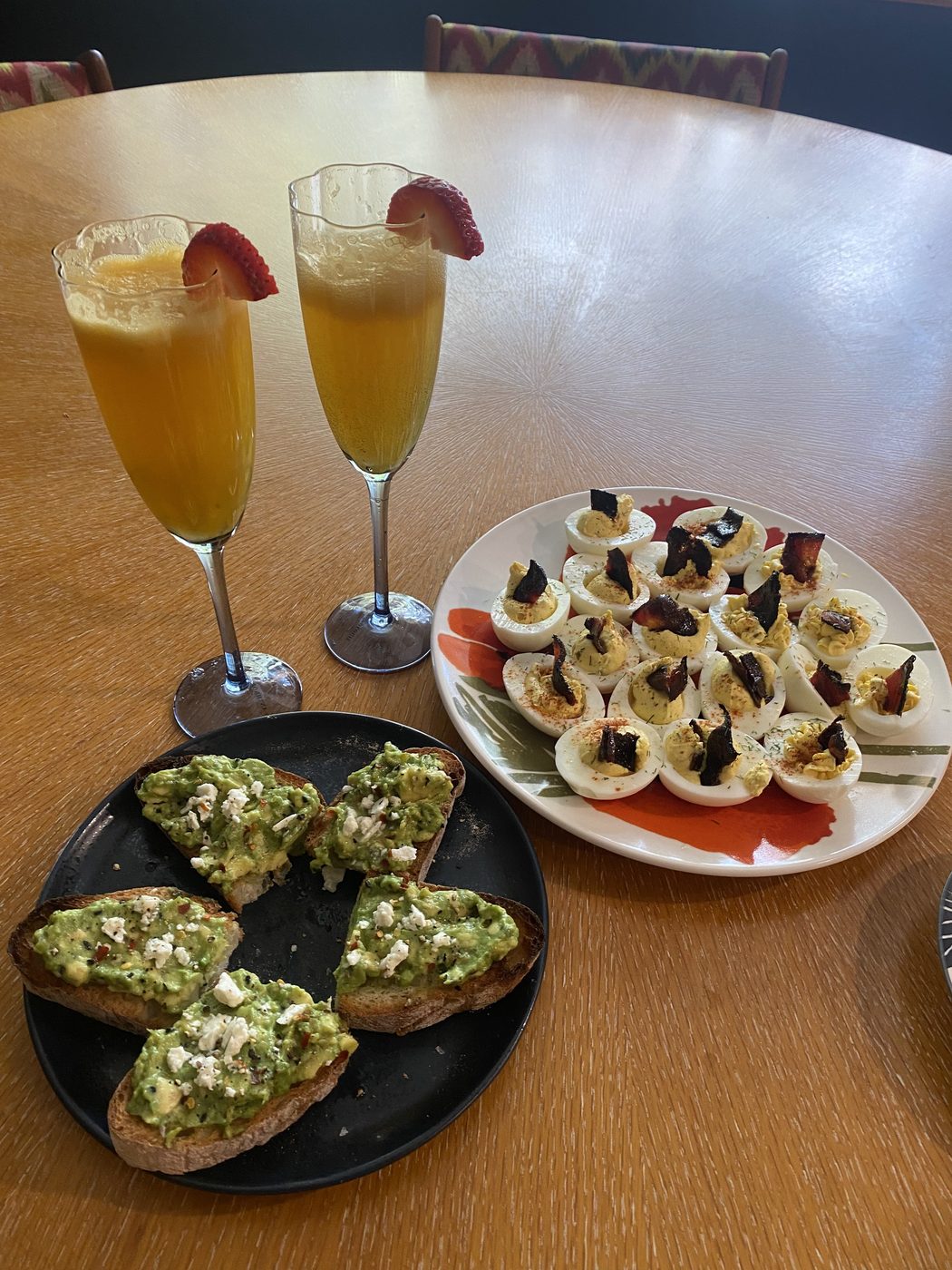 Mimosas with strawberries beside deviled eggs and avocado toast.