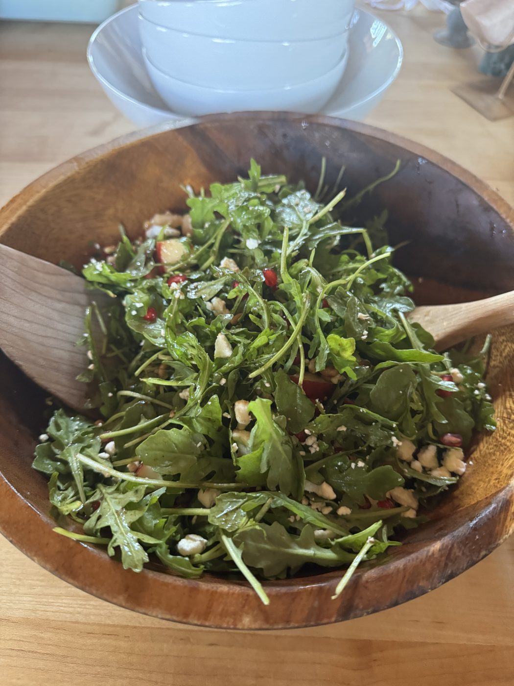 A wooden bowl of arugula salad with white beans and pomegranate.