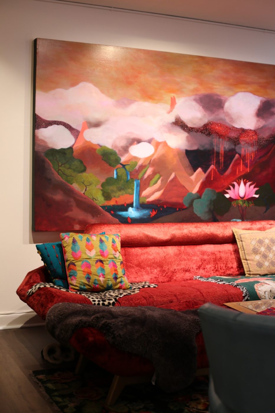 A lounge with a red sofa beneath Amy’s large red mountain painting.