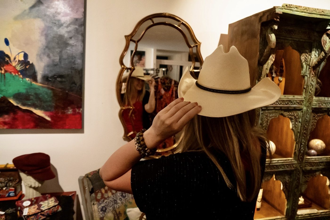 A guest trying on a straw cowboy hat in front of an ornate mirror.
