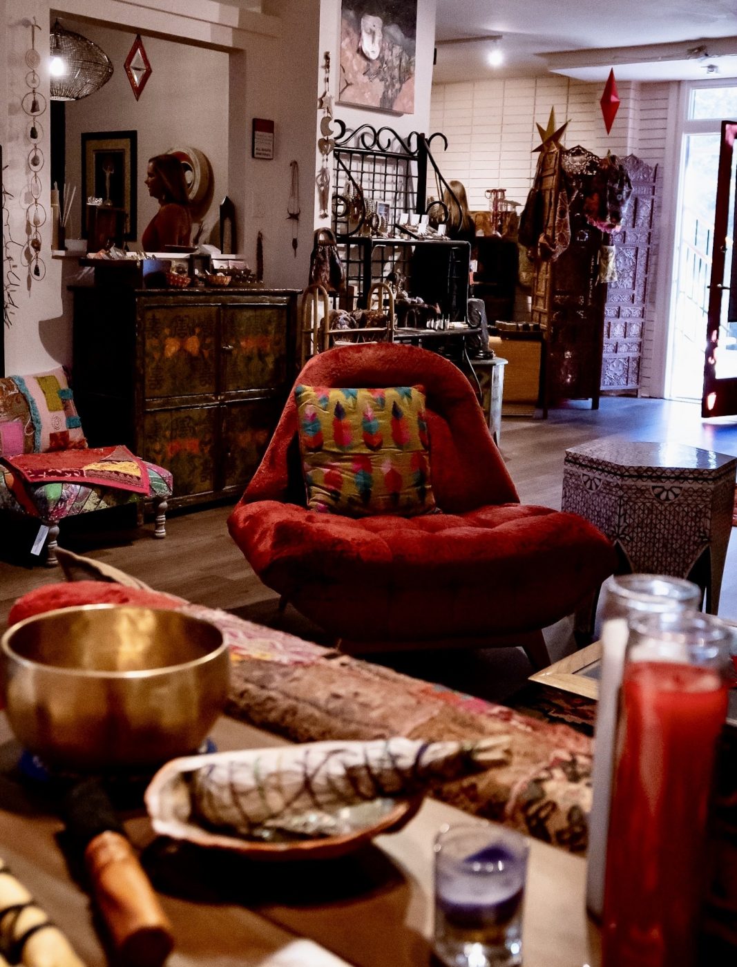 The Goddess Gatherings lounge with a red armchair, singing bowl, candles and sage.