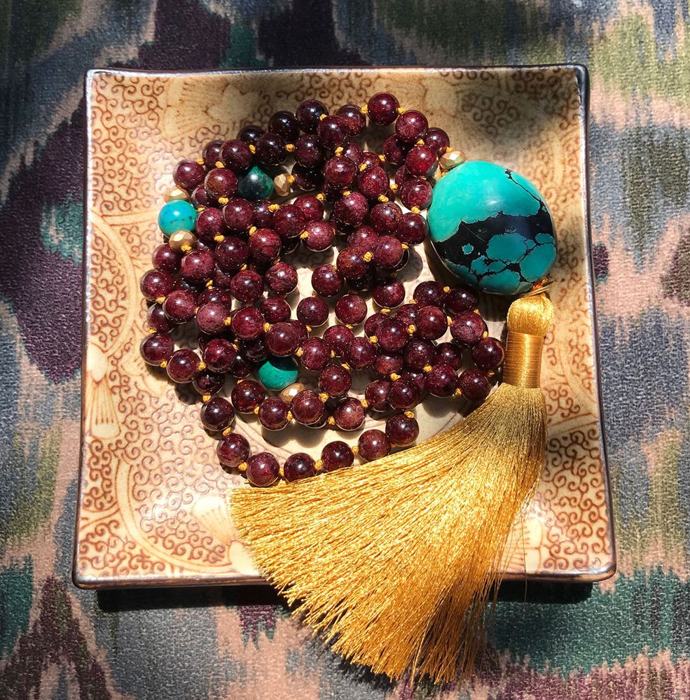 Deep red bead mala with a turquoise stone and a gold tassel.