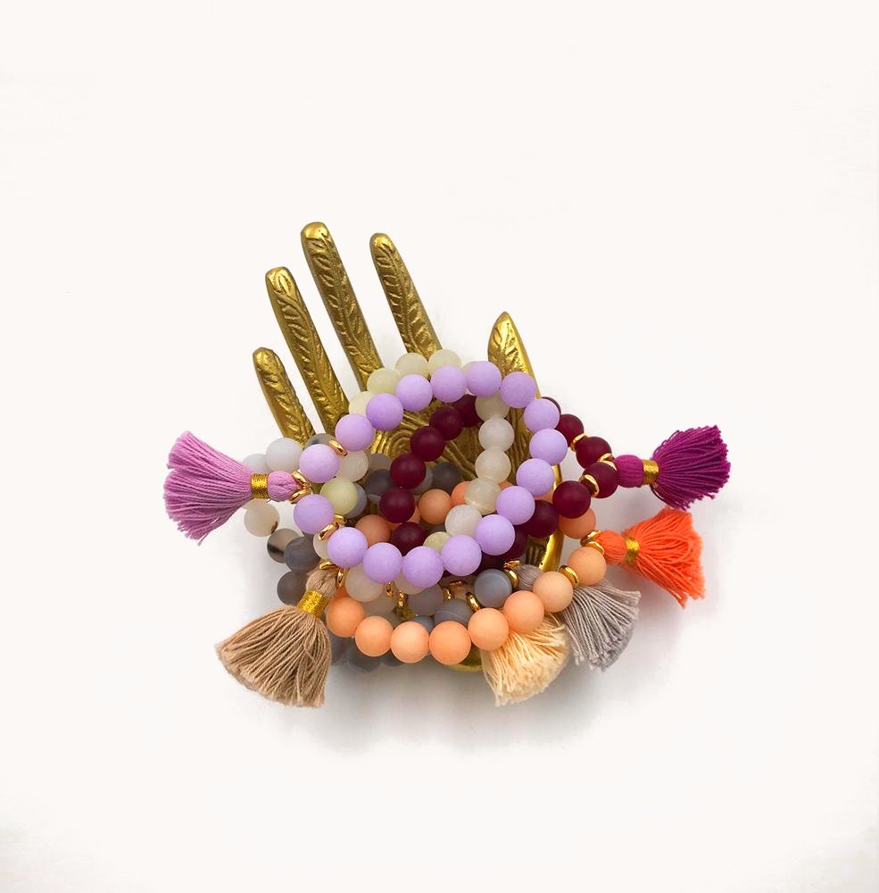 Colorful bead bracelets with tassels on a gold hand.