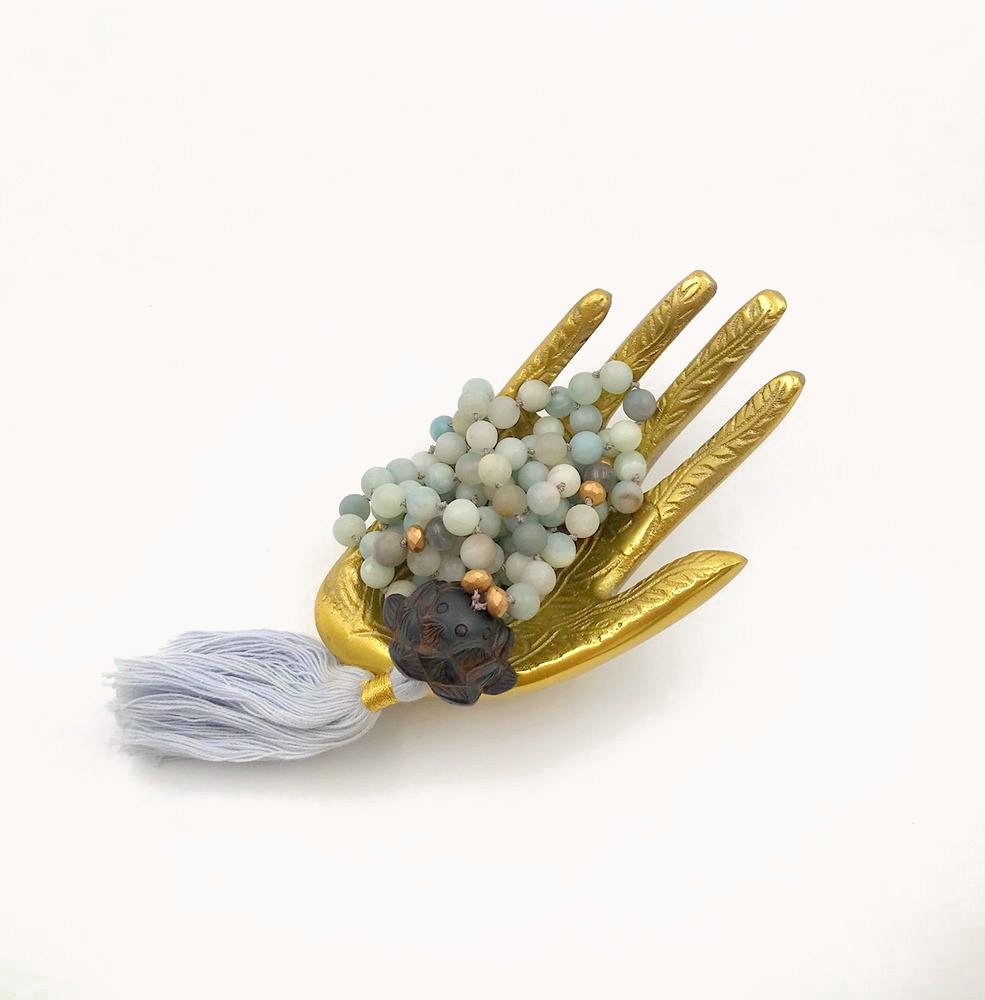 Stack of pale stone bracelets on a gold hand with a white tassel.