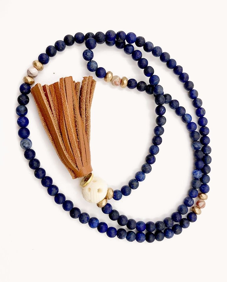 Lapis bead mala with gold accents, a carved bead and a tan leather tassel.