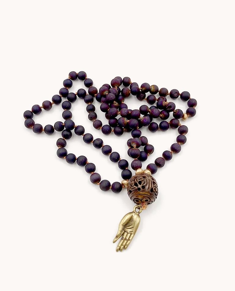 Purple bead mala with a carved bead and a small brass hand charm.