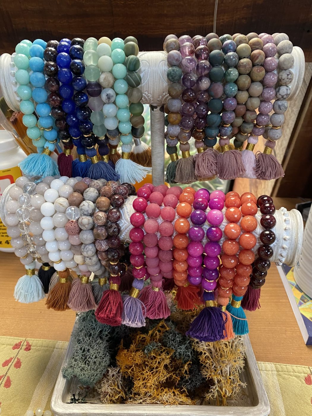 Rows of gemstone bracelets with tassels on a wooden display.
