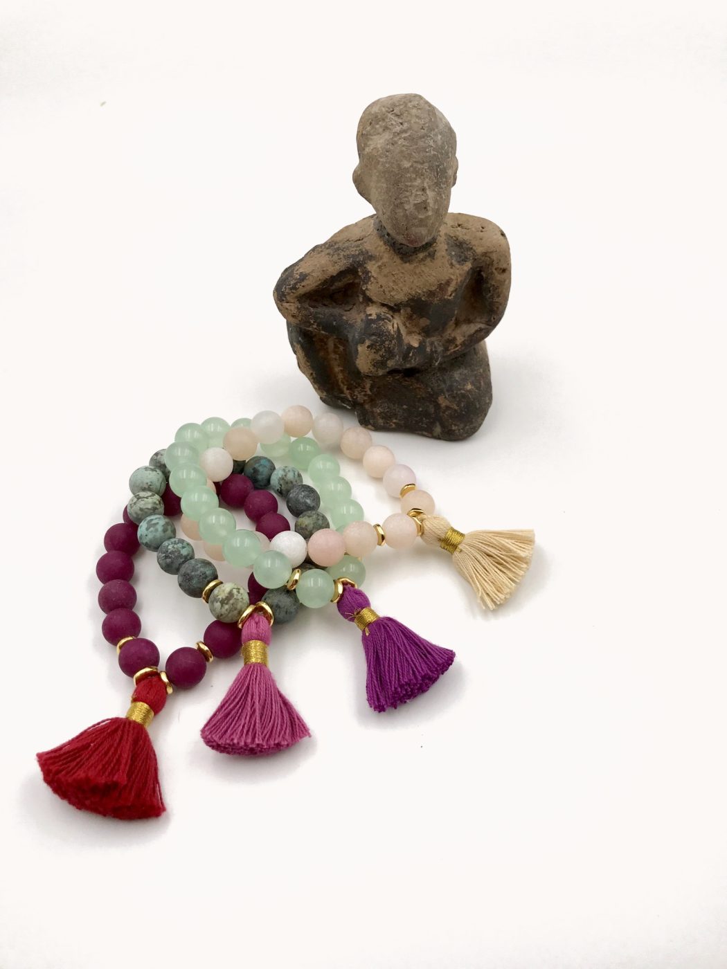 Three bracelets with red and magenta tassels beside a carved stone figure.