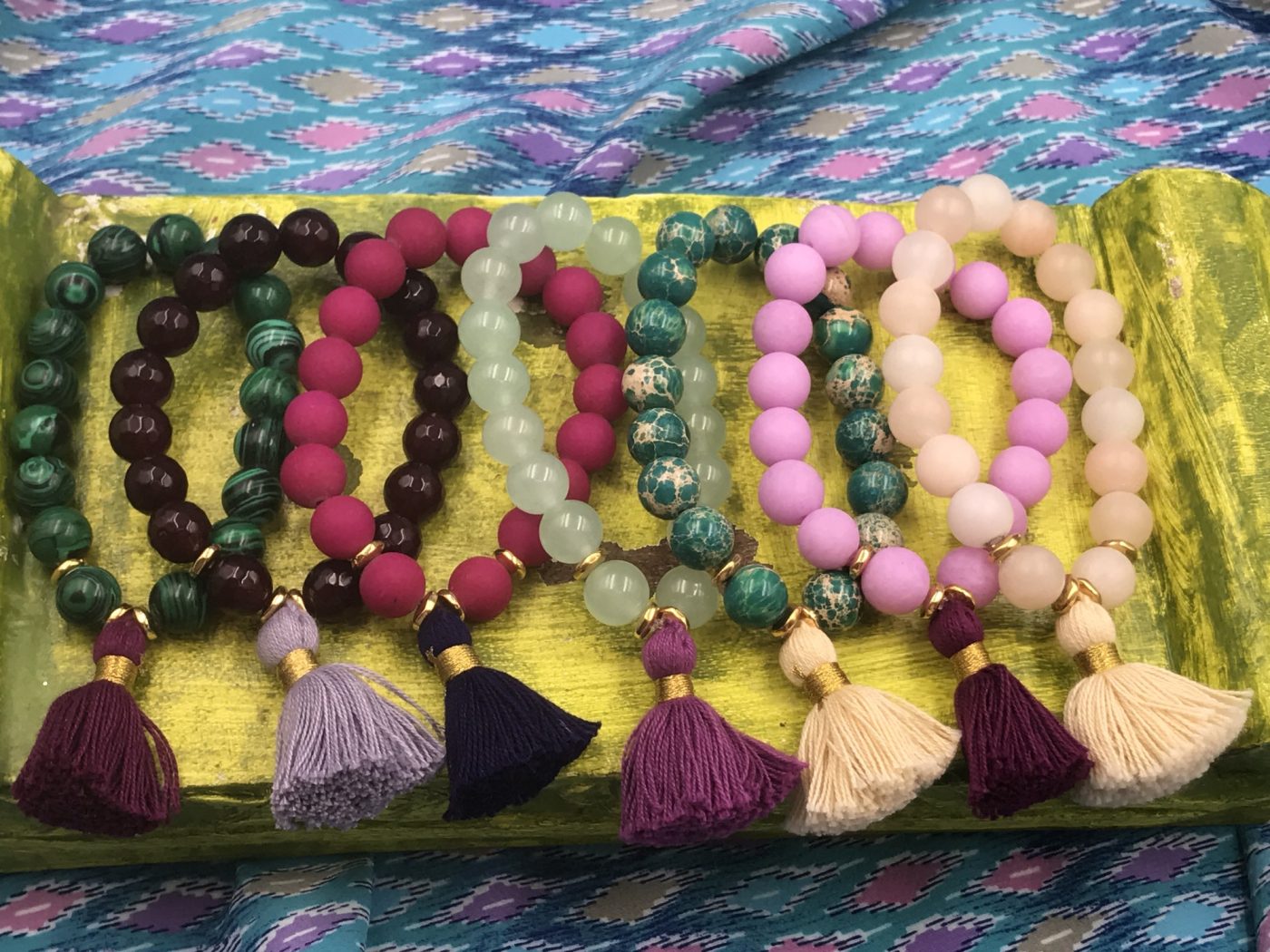 A row of tasseled bracelets in plum, pink and green laid on yellow silk.