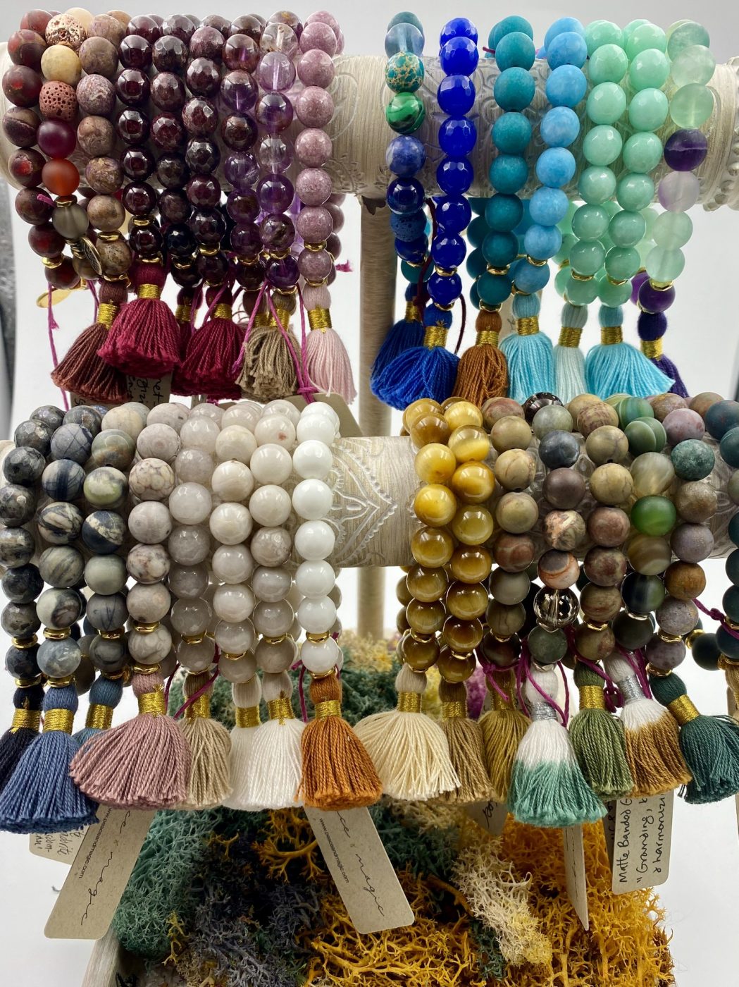 A display of gemstone bracelets with tassels and handwritten tags.