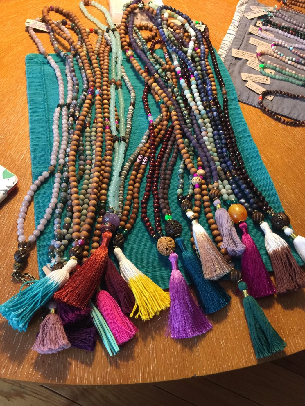 Many tasseled malas laid out on a teal cloth.