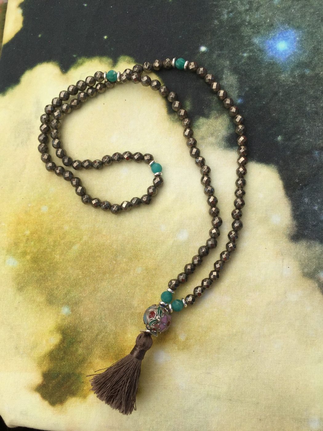 A dark bead mala with a brown tassel on a golden painted background.