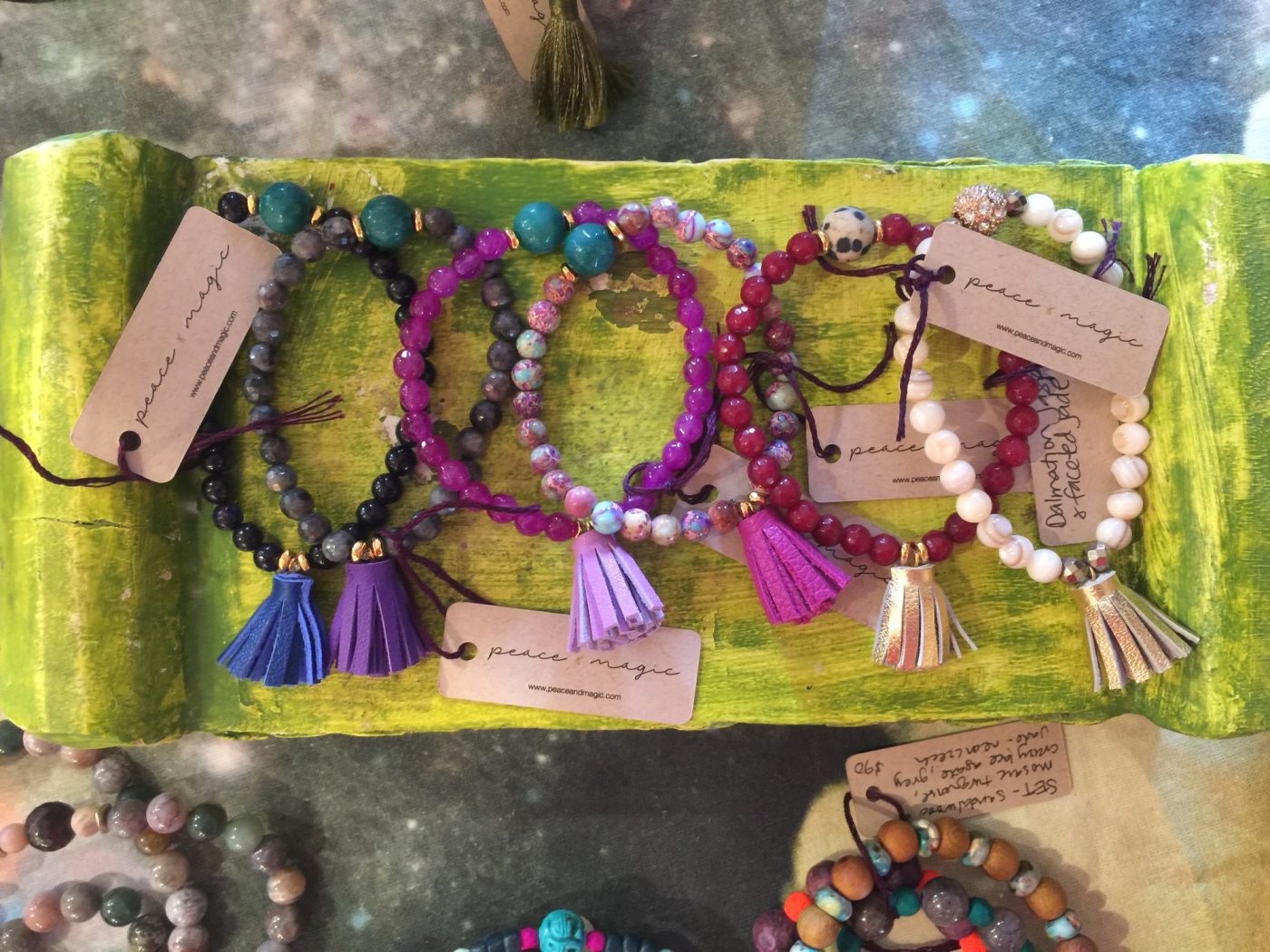 Tasseled bracelets with paper tags on a green velvet scroll.