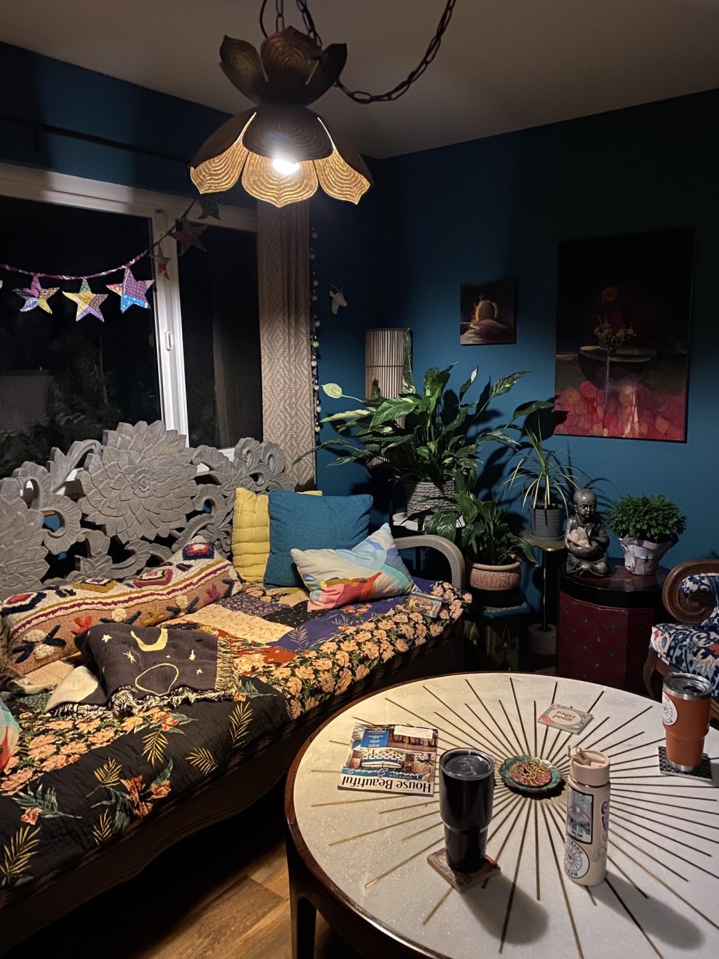 A cozy room with a flower lamp, star garland, plants and a patterned daybed.