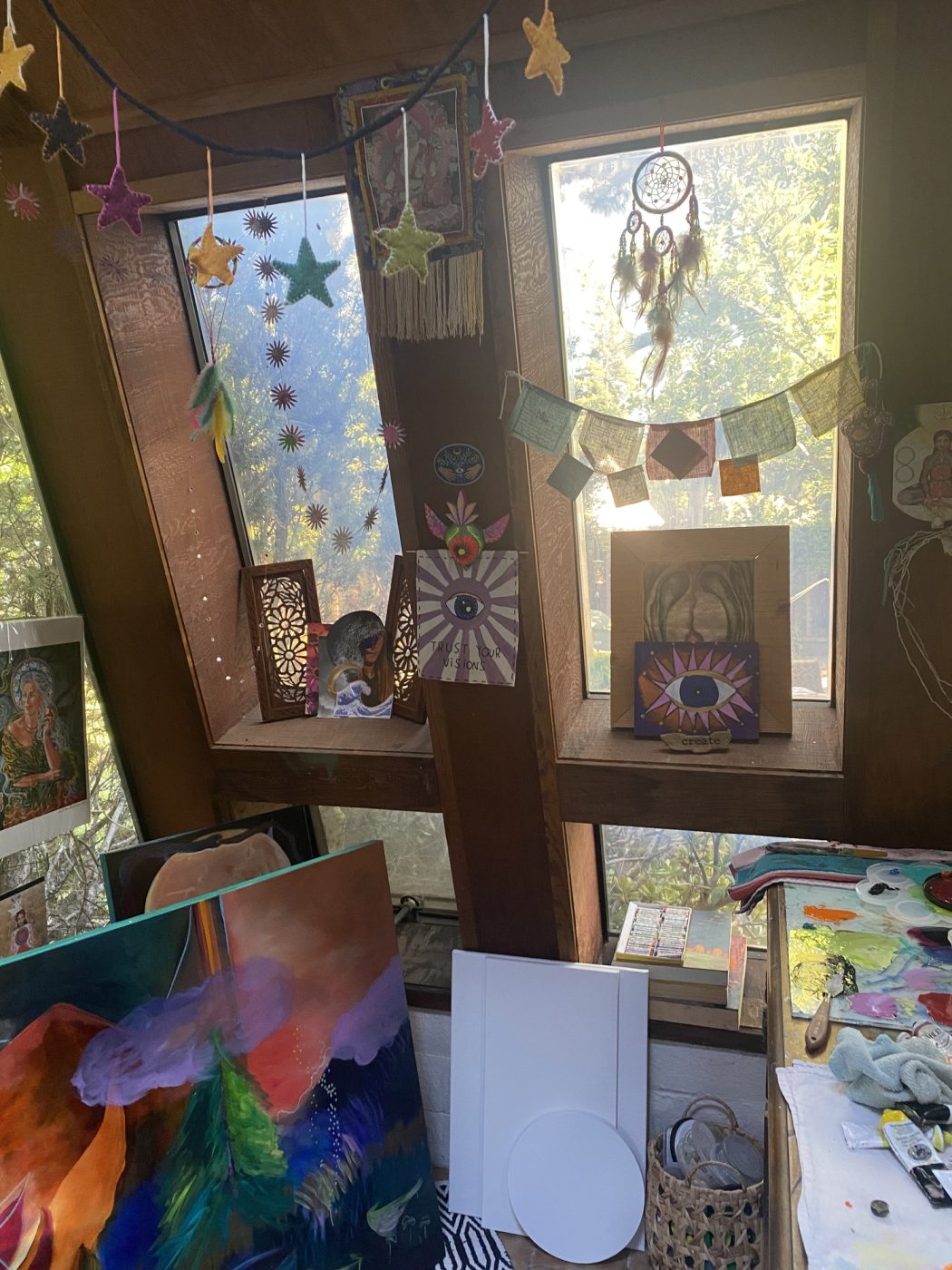 A studio window hung with prayer flags, stars and a dreamcatcher.