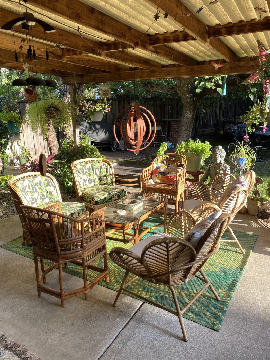 A shaded patio with rattan chairs, potted plants and hanging chimes.
