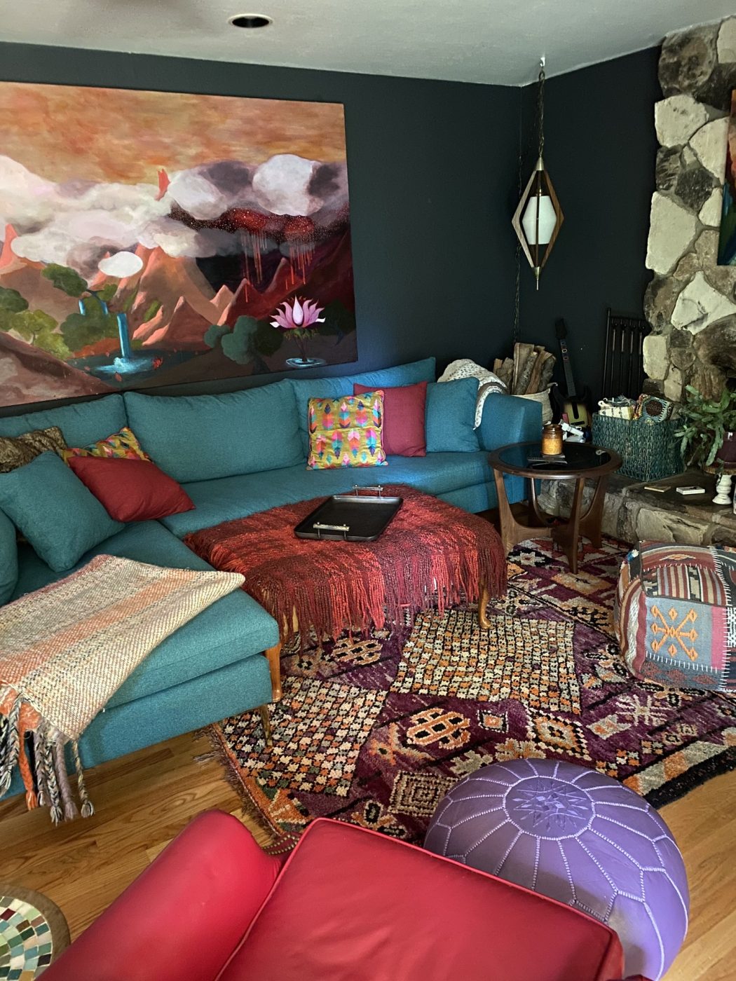 A teal sectional and layered rugs beneath a large red mountain painting.