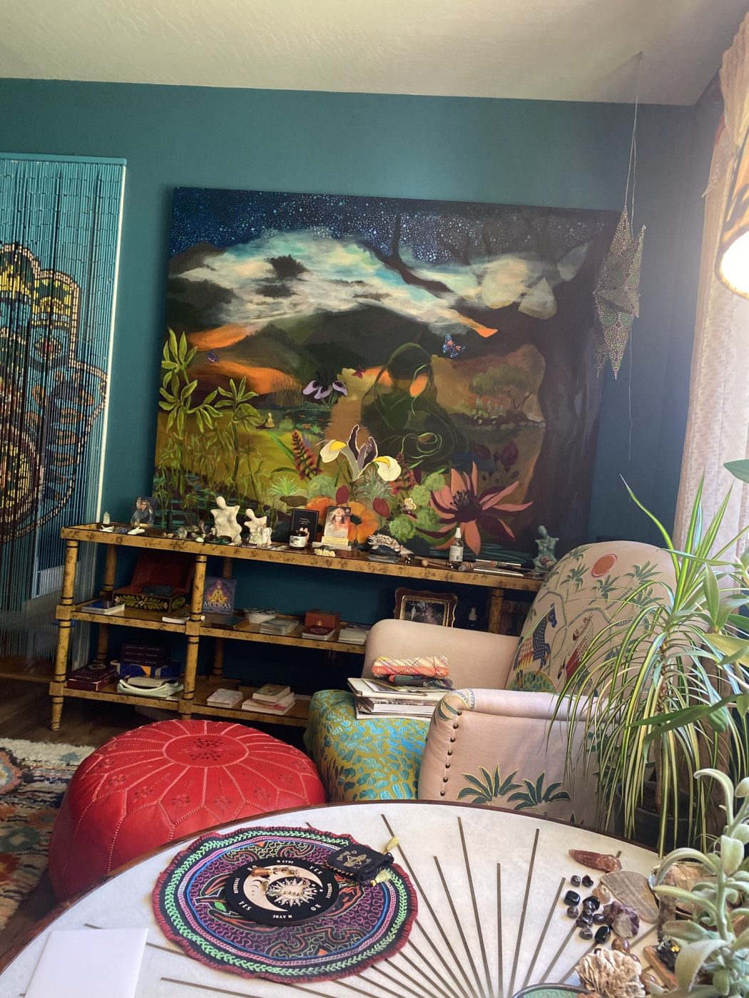 A dining corner with a night landscape painting, red pouf and potted plants.