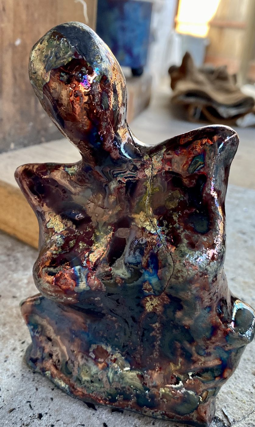 A raku goddess in deep copper, red and gold lustre, with a slender head and winged shoulders.