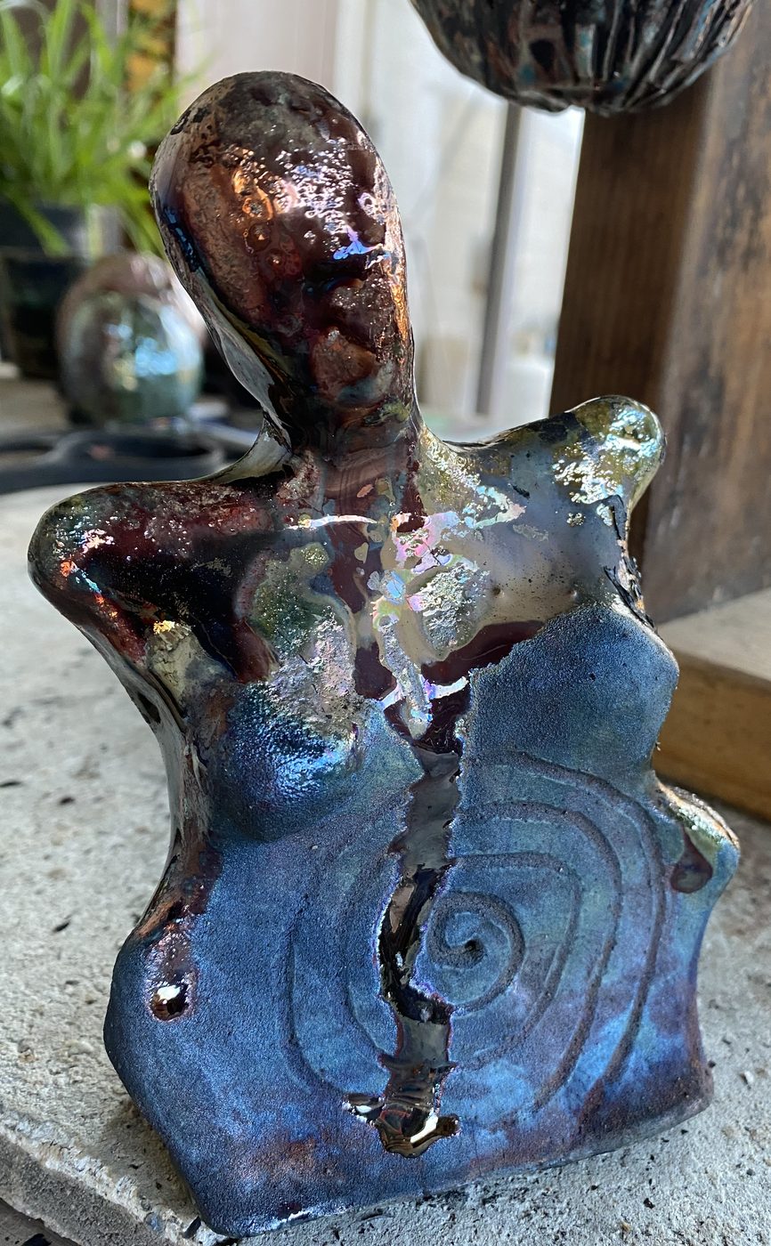 A raku goddess in copper and blue with a spiral carved into her belly and a gold-filled seam running down her body.