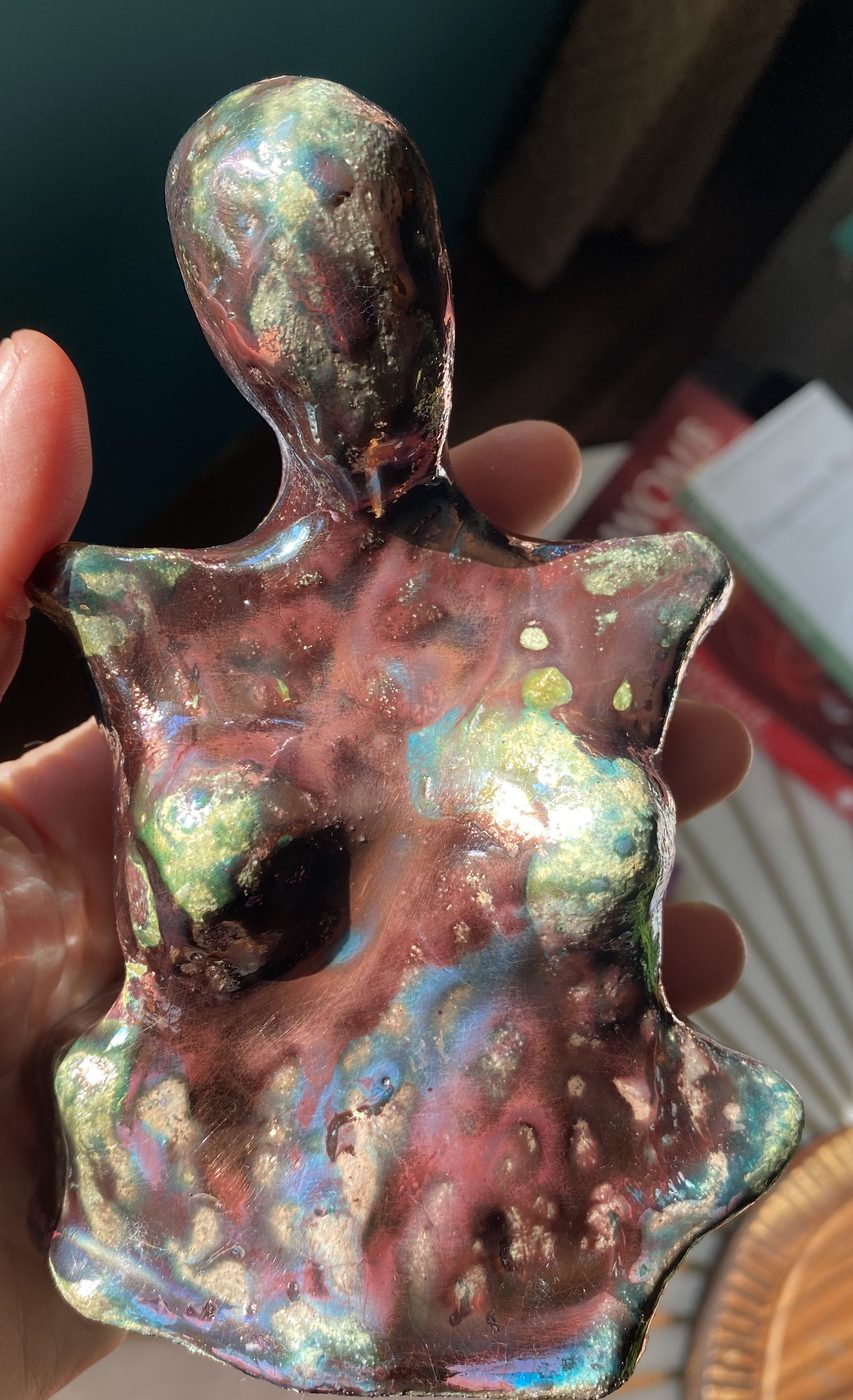 A small raku goddess held in the hand, in pearly pink, green and gold lustre.