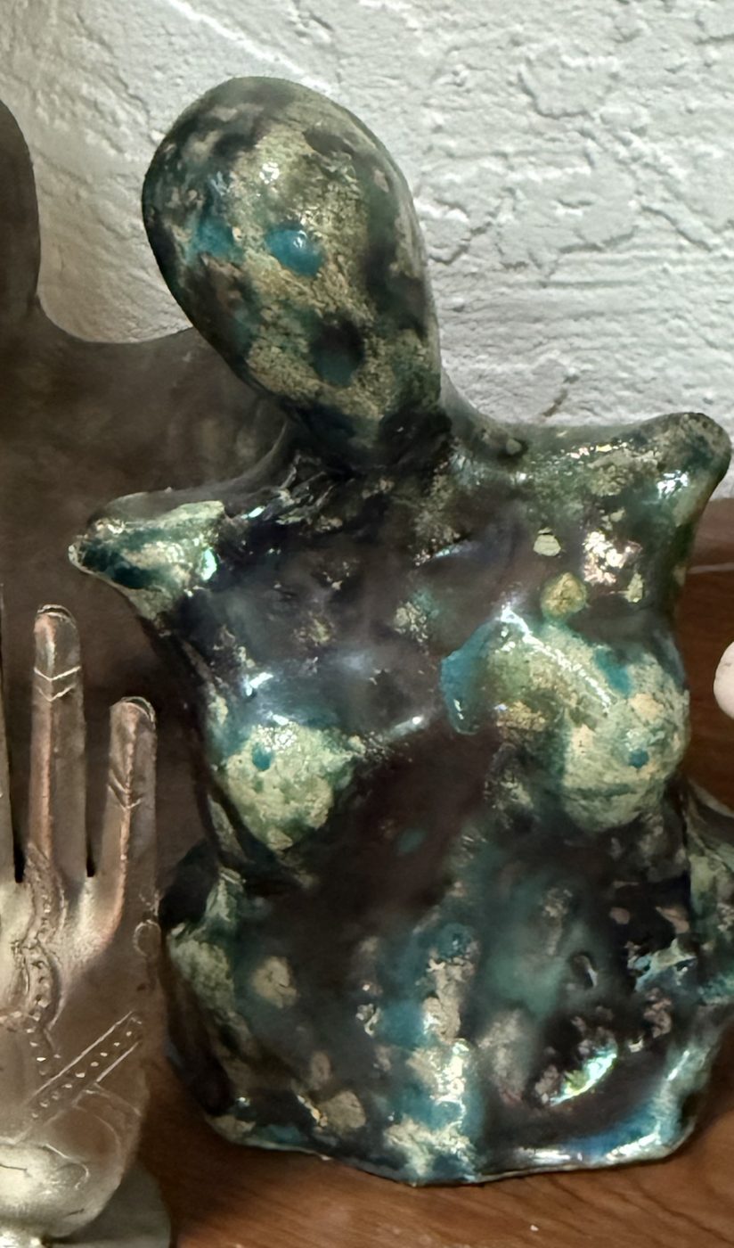 A raku goddess torso in deep blue, teal and gold glaze, beside a small silver hand.