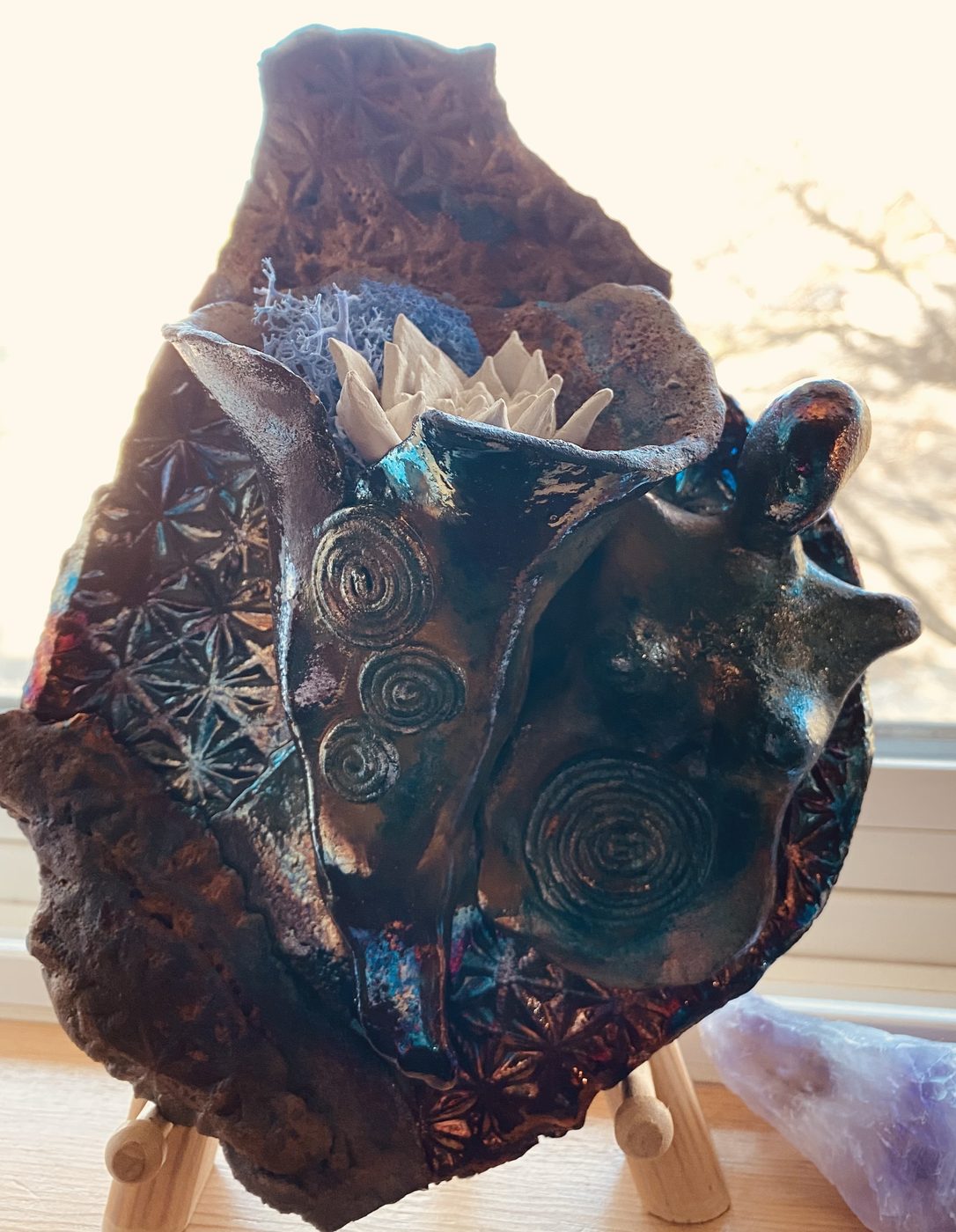 A ceramic wall piece: a goddess with spiral-stamped breasts and a cluster of white crystals, on a stamped clay ground in deep blue and copper.