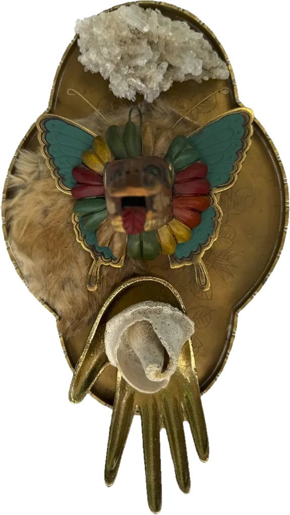 A brass tray with a crystal cluster, a carved feathered mask on butterfly wings, fur, and a brass hand holding a shell.