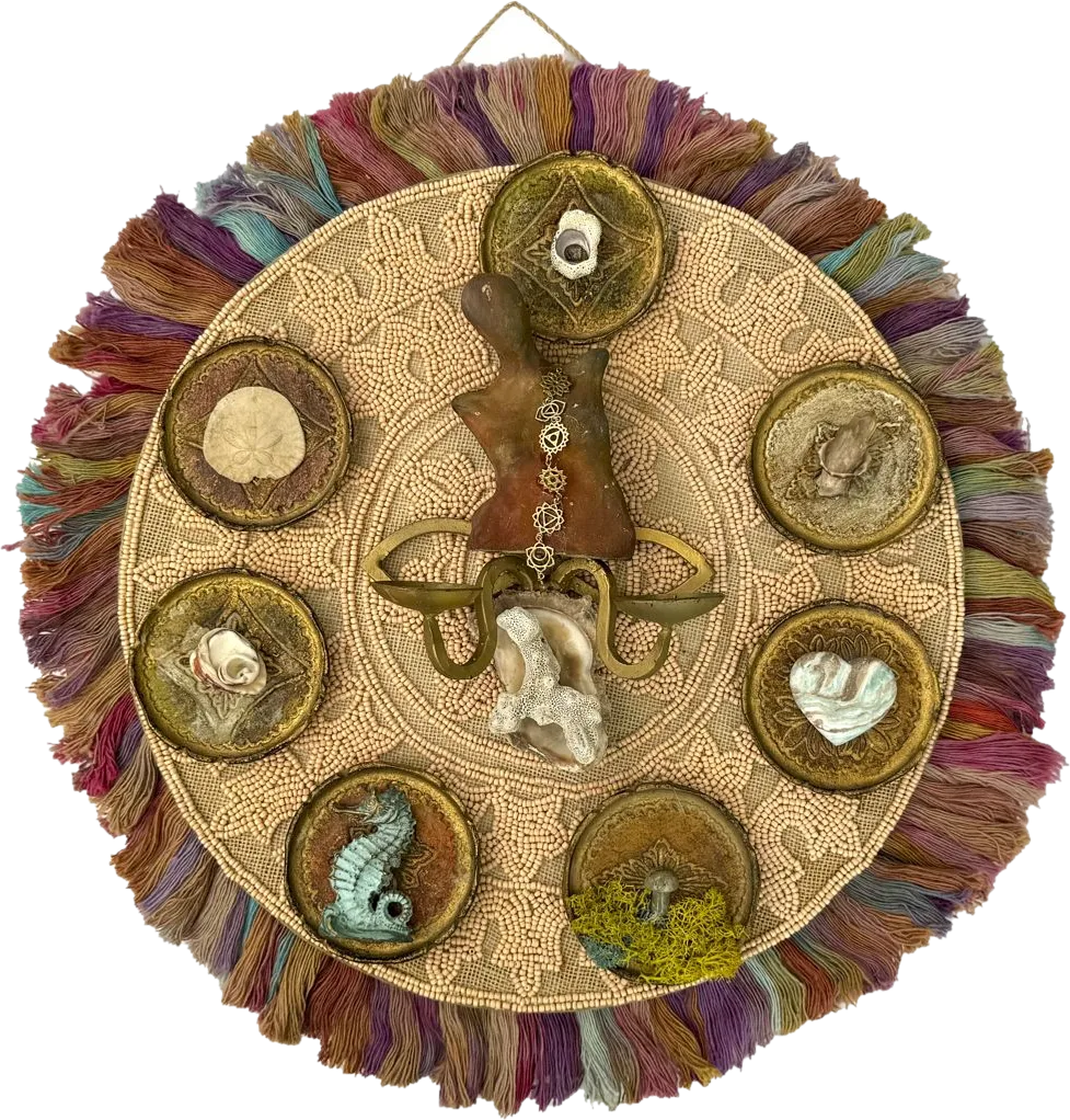 A round beaded mandala with hand-dyed fringe, a central figure wearing a chakra chain, and seven brass dishes holding shells, a seahorse, a heart stone and a mushroom.