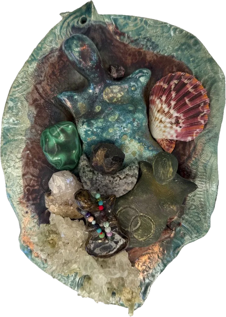 A raku ceramic dish holding a goddess figure, malachite, a scallop shell, crystals and a small beaded figure.