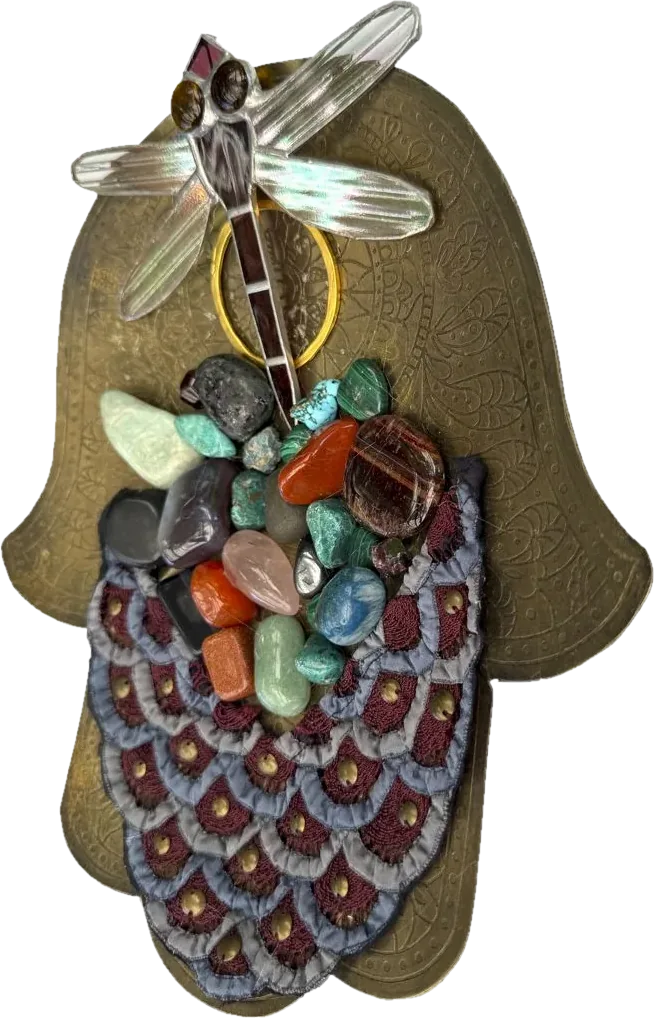 An etched brass hamsa with an embroidered scalloped crown, a cluster of tumbled stones and a stained glass dragonfly.
