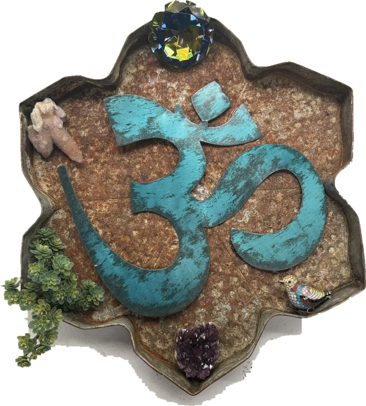 A turquoise Om symbol in a rusted lotus-shaped tray, with a faceted crystal, a quartz cluster, an amethyst, a cloisonné bird and trailing succulents.