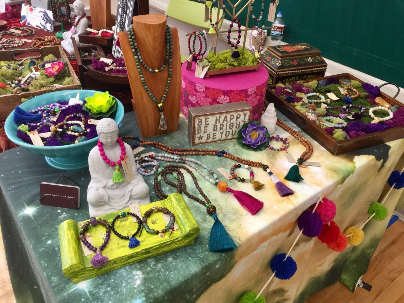 Bracelets in bright trays beside a white Buddha on a floral cloth.