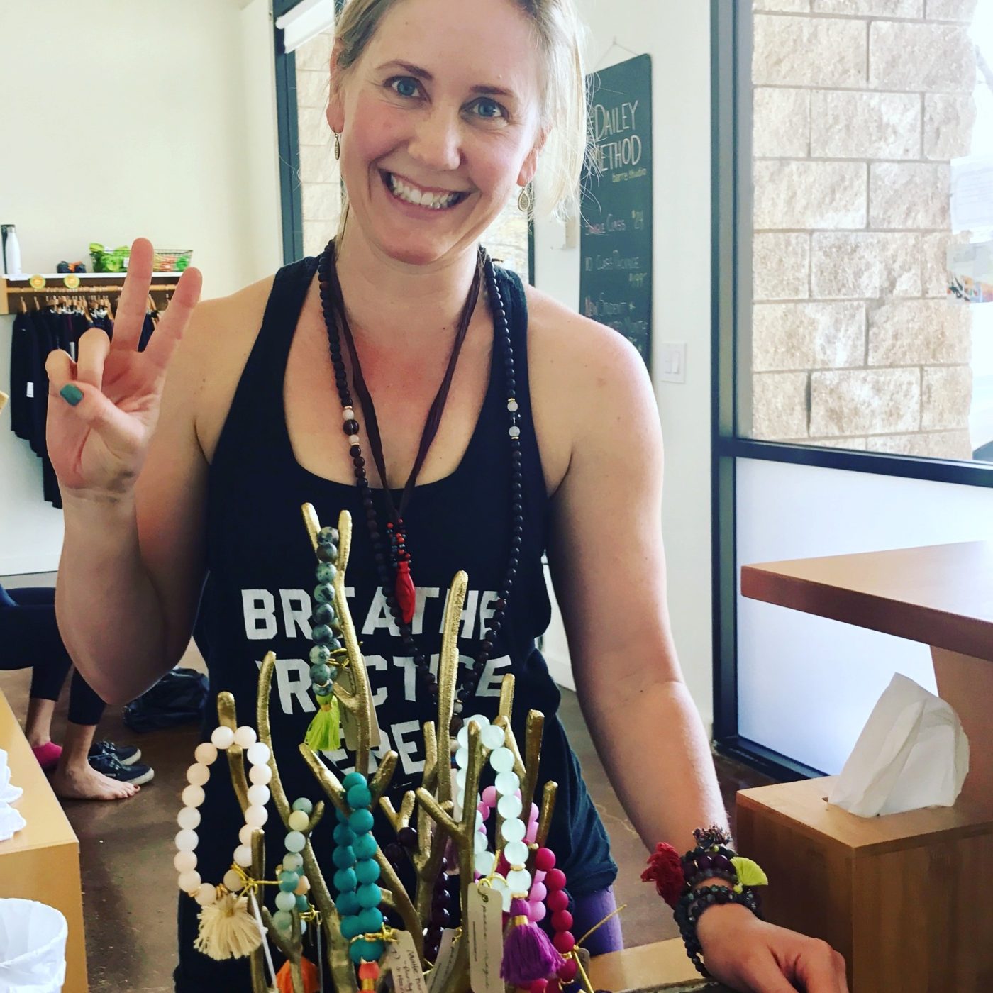 Amy giving a peace sign behind a branch display hung with malas.