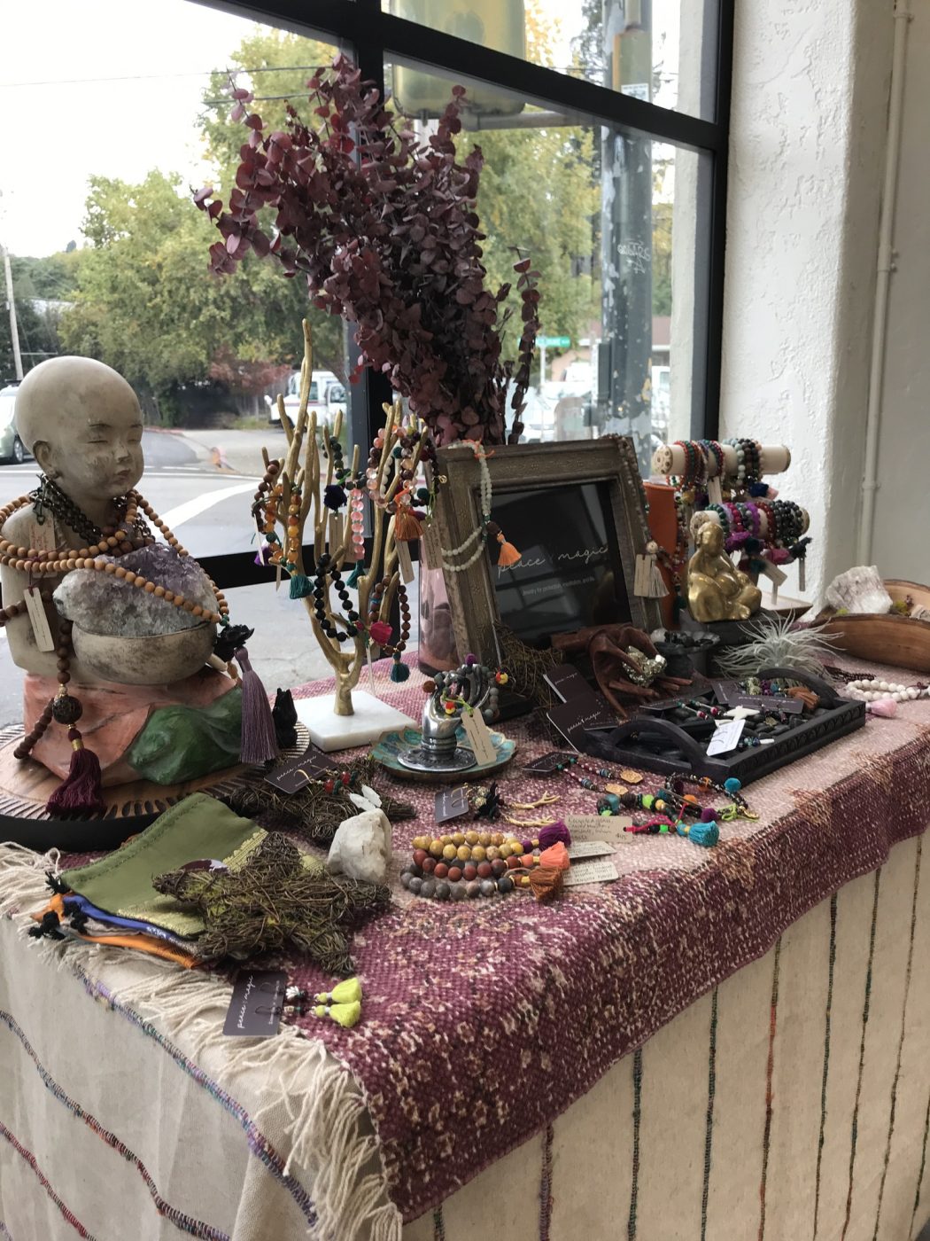 A pop up table with a small Buddha, jewelry and dried flowers on layered textiles.