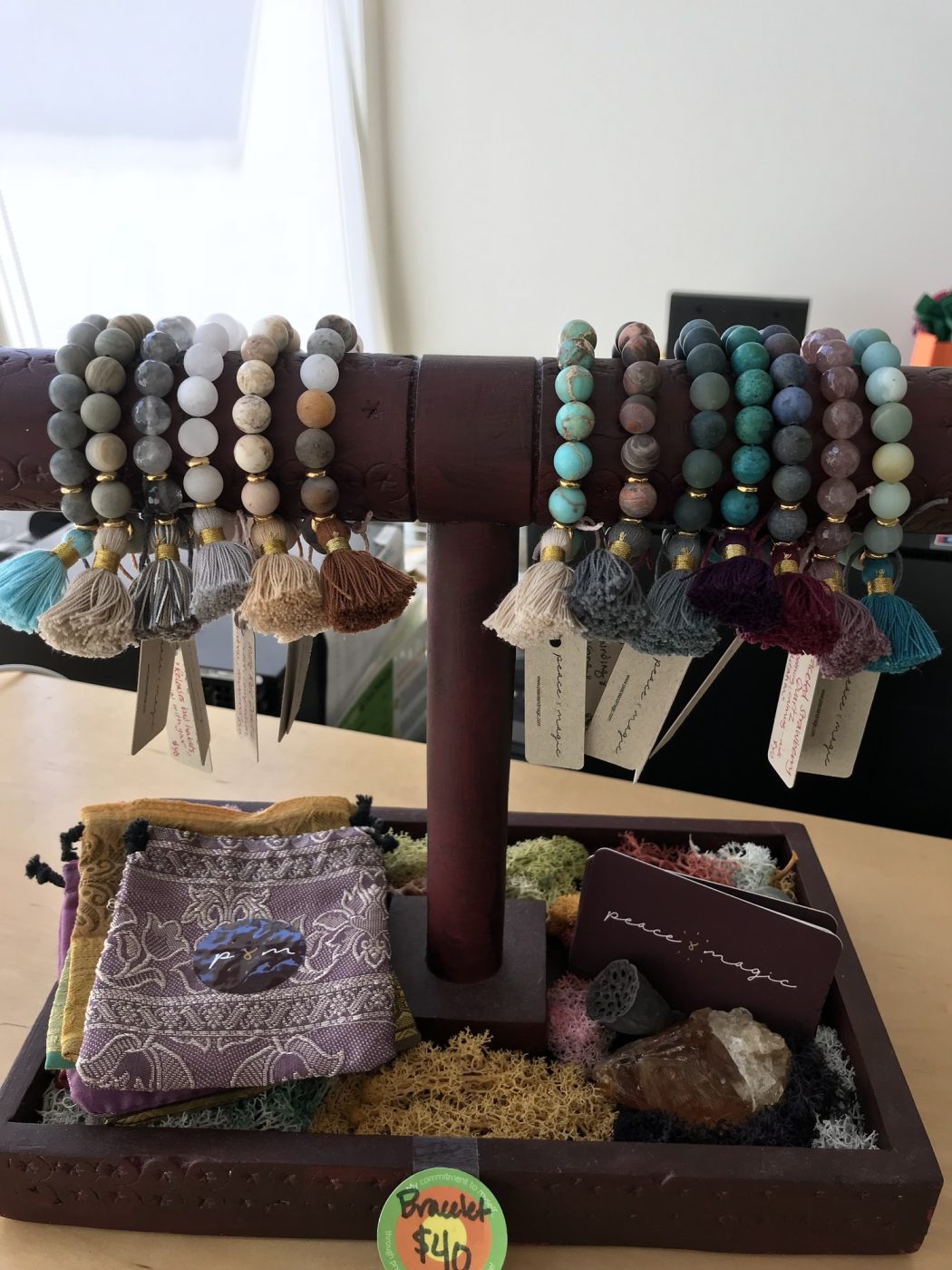 Tasseled bracelets on a wooden stand above a tray of crystals.