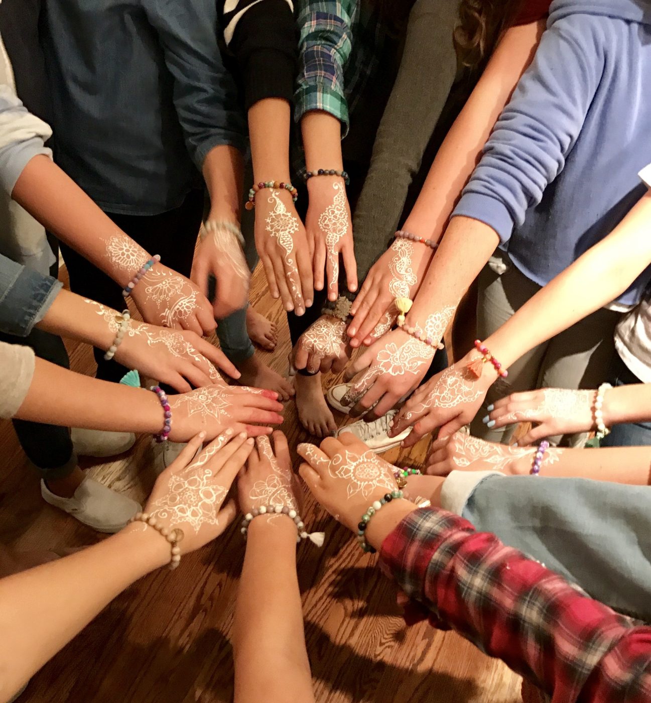 Many hands joined in a circle, decorated with fresh henna.