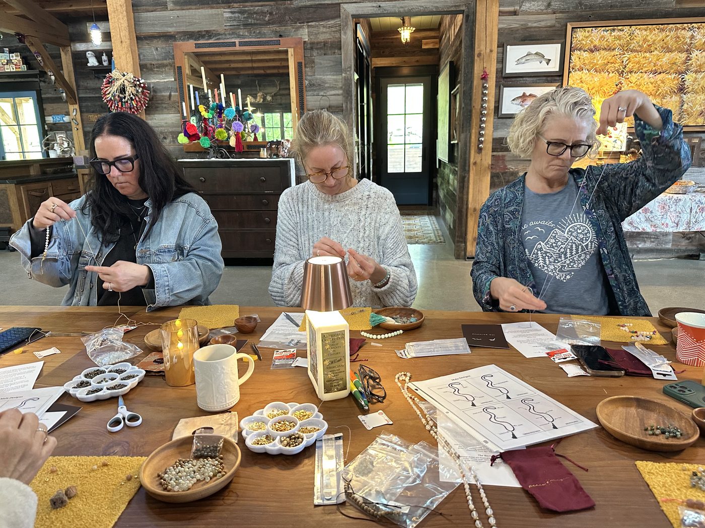 Women making malas around a long table in a barn workshop.